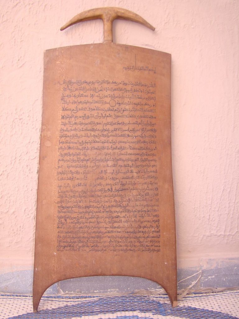 A red-brown plaque with legs contains surat from the Quran written in the Hausawi script.