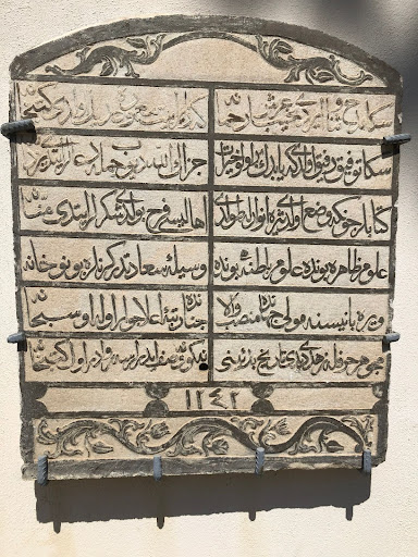 Ottoman inscription engraved into limestone and hung on the cream-colored outer wall of the library. The last line of the inscription shows the Hijri year 1241 and the inscriptions are framed by floral patterns.