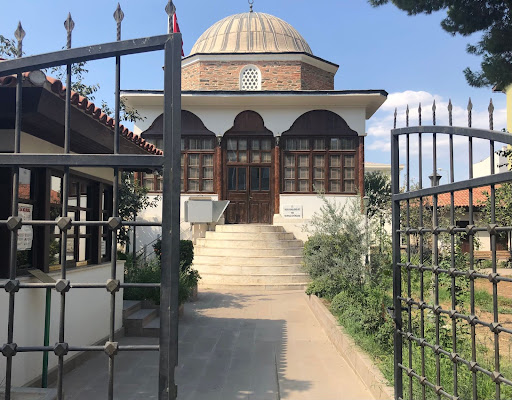 The library, a brick structure with a dome and wooden portico, is situated in the middle of a garden seen beyond iron grates. Immediately to the left through the iron gates lies the small security booth where visitors to the library must announce themselves.
