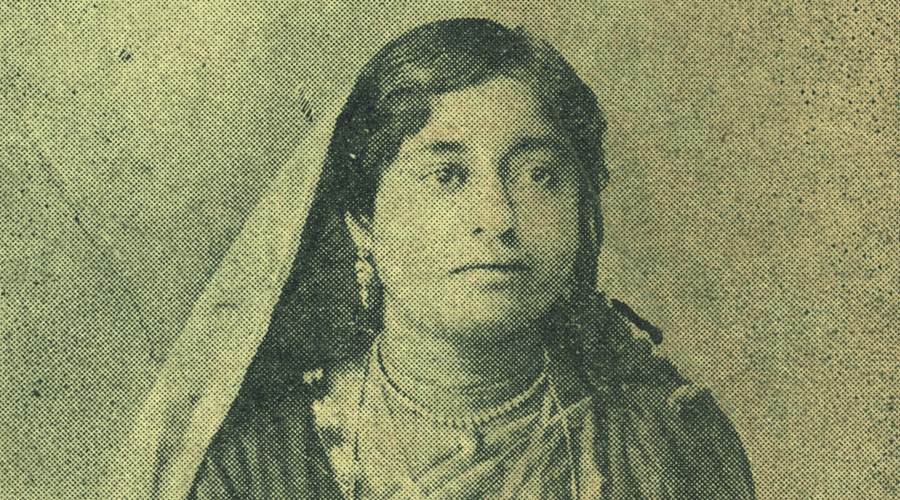 Photo of dancing girl Soshimukhi, the first voice to be recorded for the gramophone in India. Her gaze is angled beyond the camera. She is wearing a simple necklace and earrings with no other jewellery marking her lower status in the rung of performers at her troupe. She is wearing either a sari or a more casual blouse and skirt combination. Her dupatta is draped over her shoulder and covers her head. She seems to have styled her hair.
