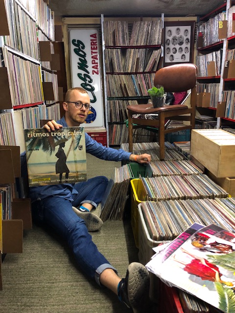The author seated on the floor at a record store, holding up a record. 